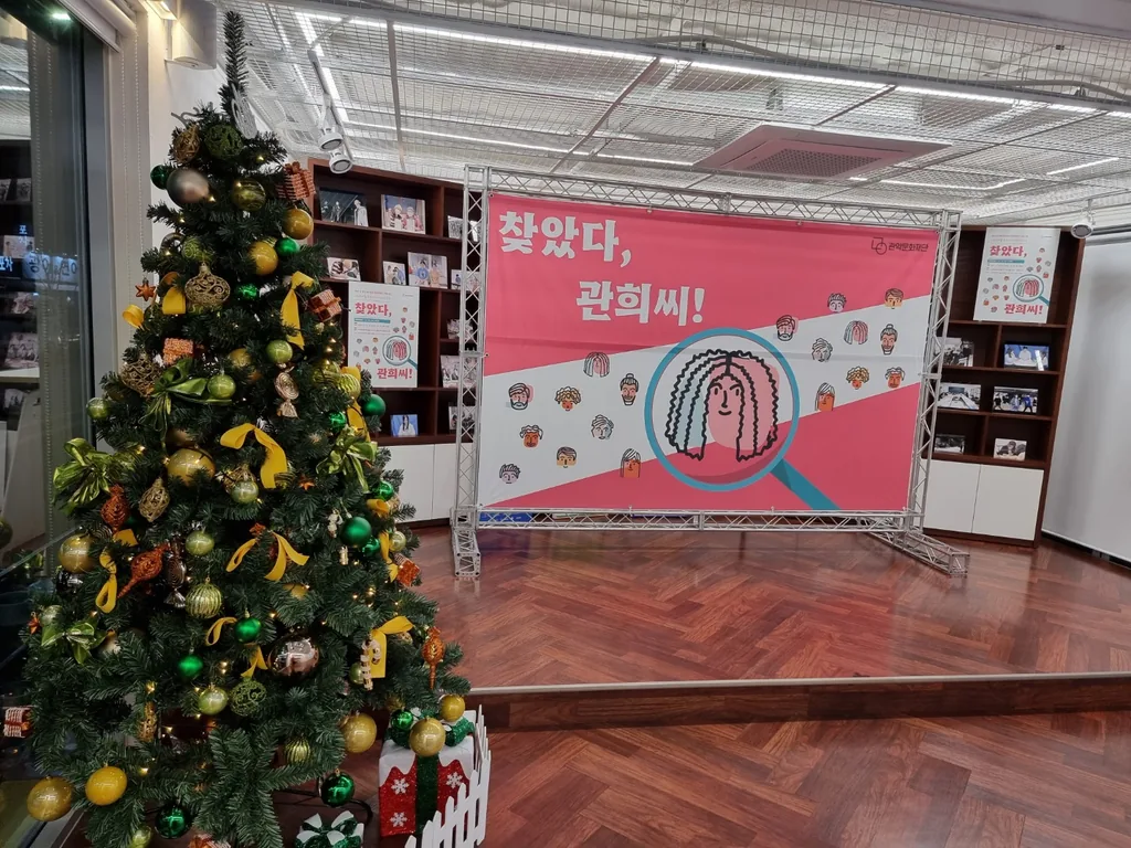 크리스마스 트리 옆 책장 앞에 세운 트러스 프레임 현수막 백월과 낮은 격자 천장