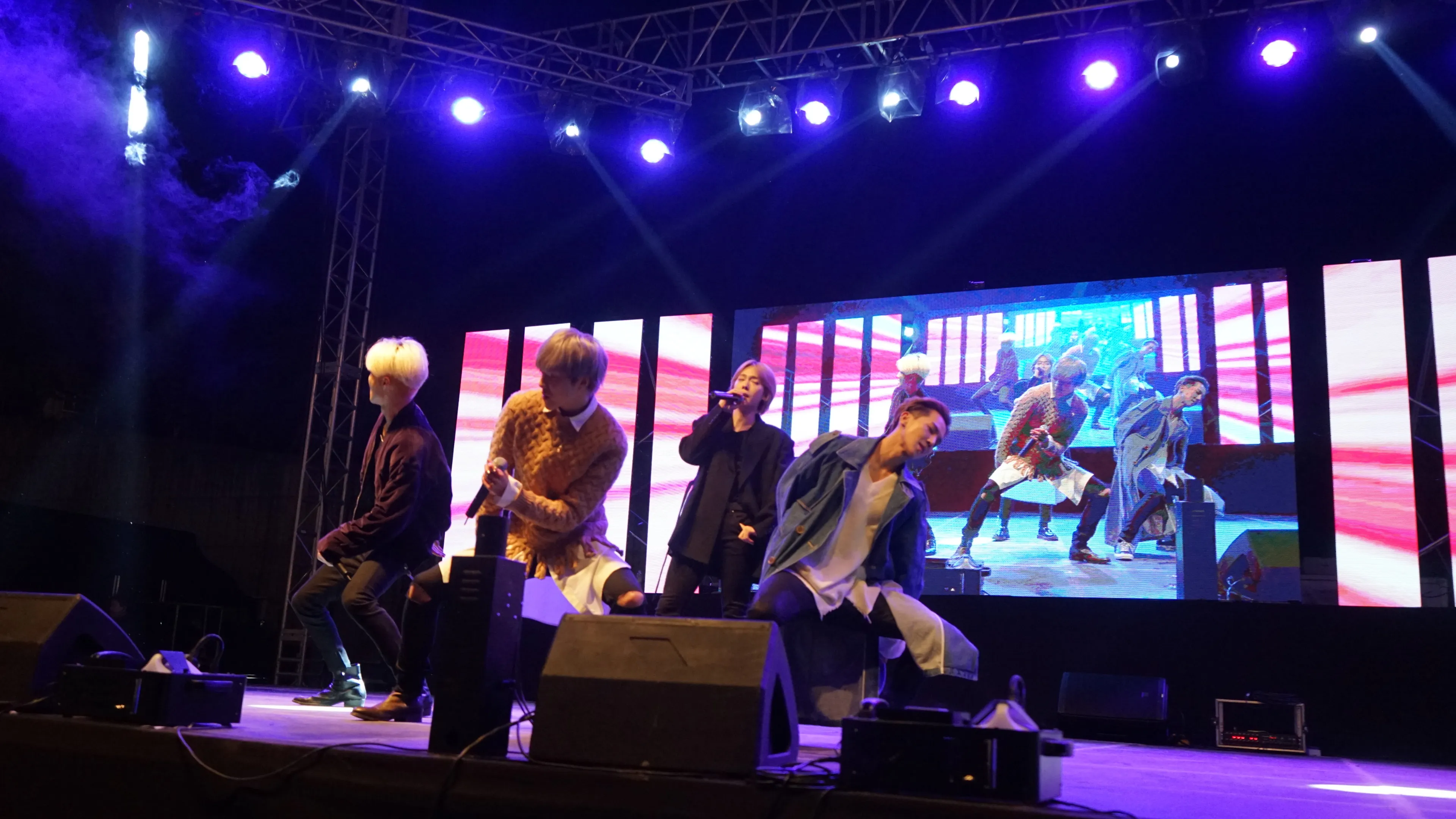보라색 무빙라이트 아래 LED 화면 앞에서 공연하는 4인조 그룹