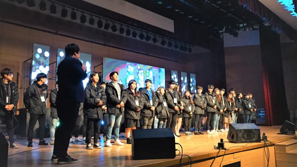 LED 화면 앞 무대에 줄지어 선 학생들과 마이크를 든 진행자