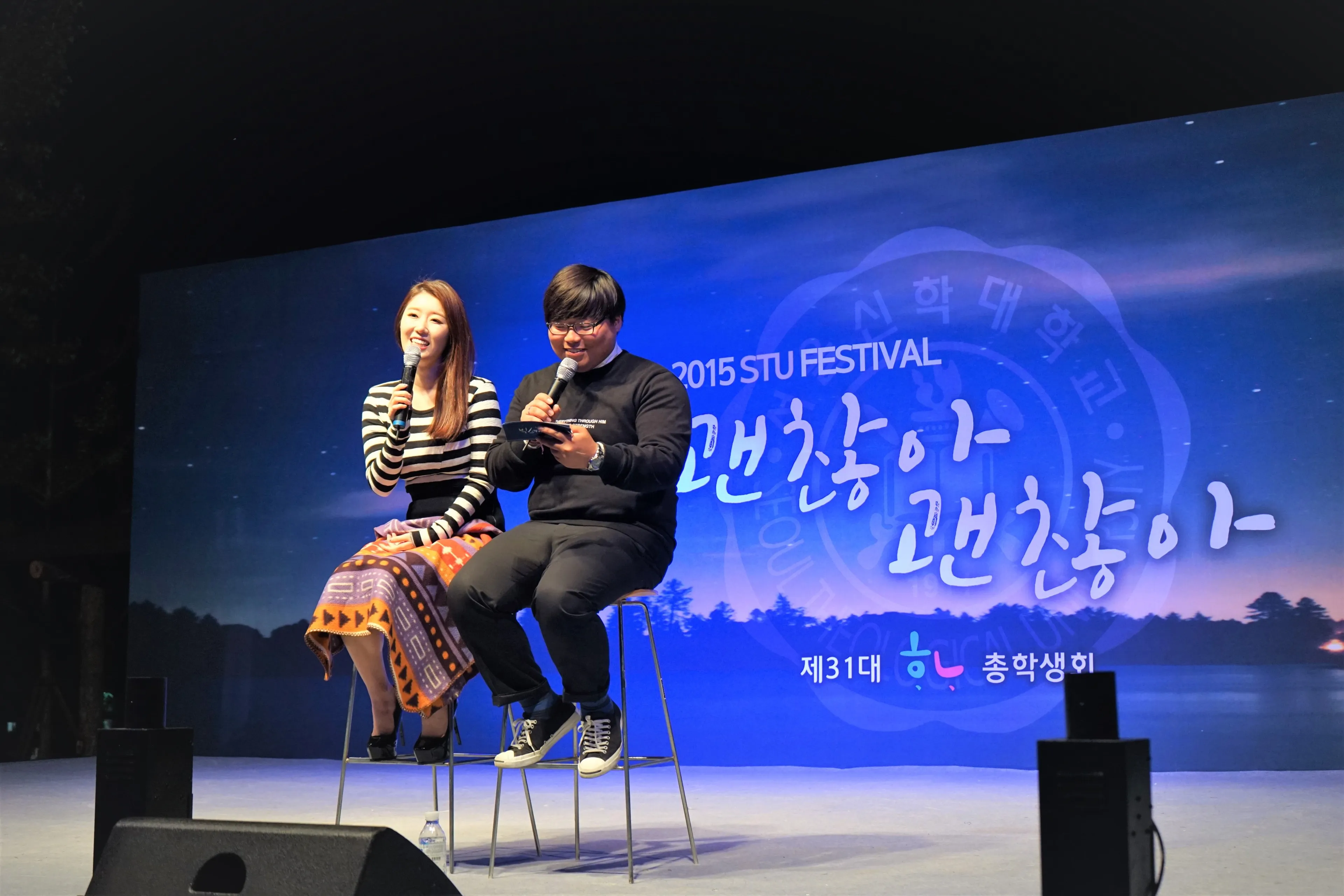 축제 백월 앞 의자에 나란히 앉아 마이크로 대화하는 두 사람