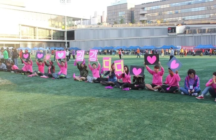 분홍 티셔츠를 입고 하트와 글자 피켓을 든 응원팀