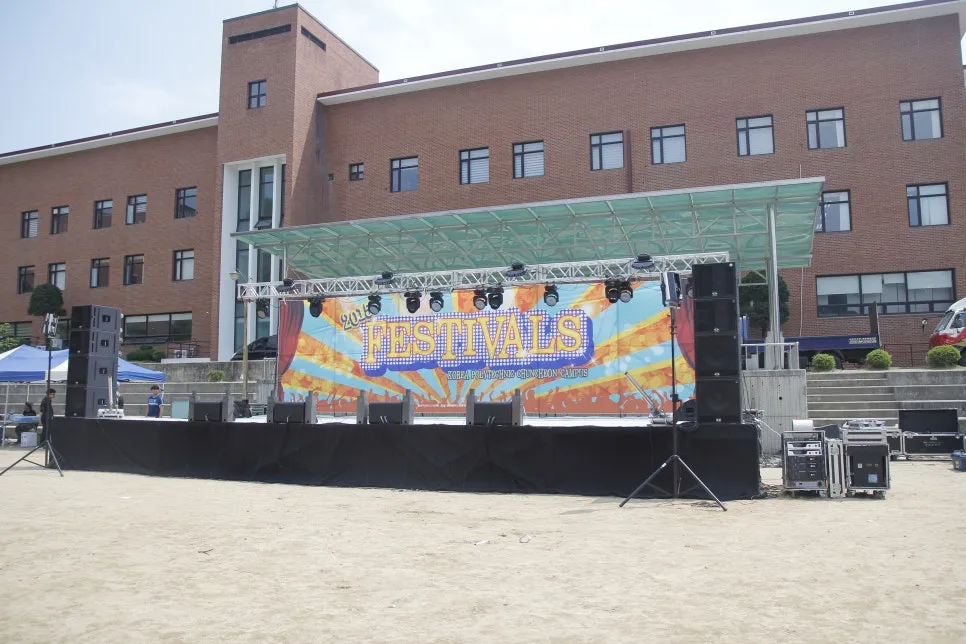 운동장 흙바닥에 세운 FESTIVALS 배경 트러스 무대와 스피커
